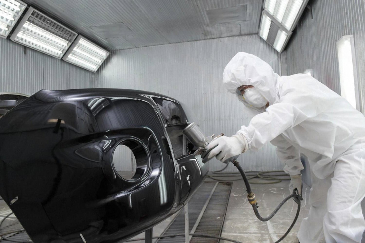 Detailer in white protective suit applying ceramic coating on a black car panel inside a UAE detailing booth