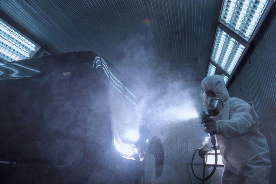 Ceramic coating being sprayed onto a car body under bright booth lighting, showing atomised SiO2 mist