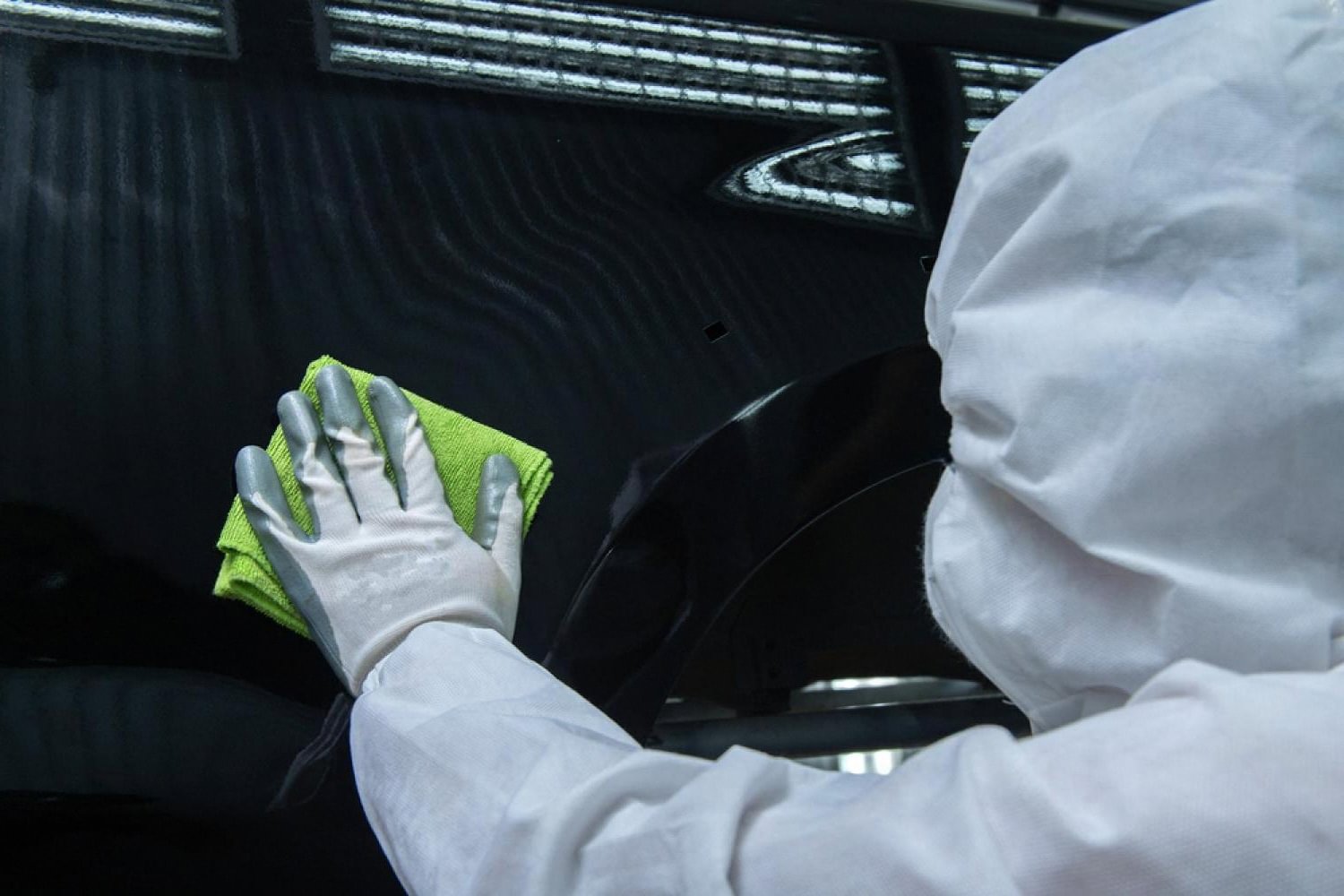 Technician buffing SiO2 ceramic coating into a car's dark clear coat with a green microfibre cloth
